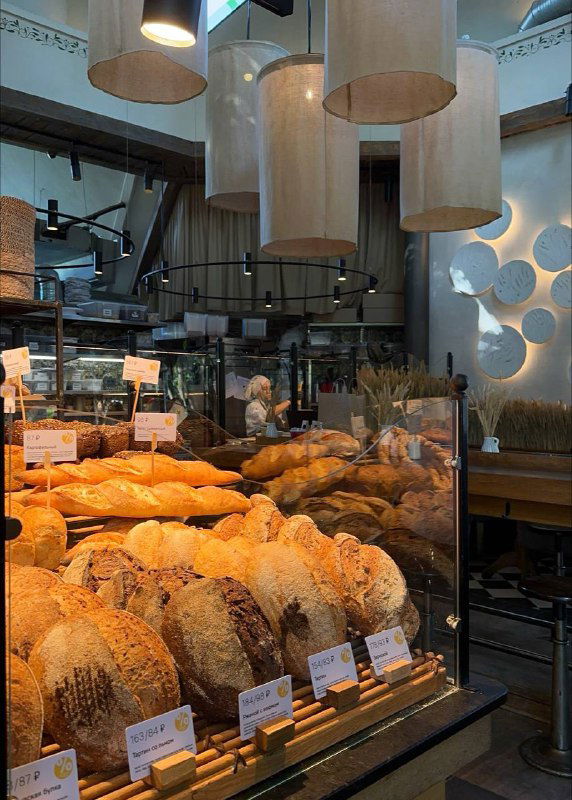 Витрина пекарни с разнообразными хлебобулочными изделиями и тёплым освещением — прилавок с свежим хлебом и булочками.