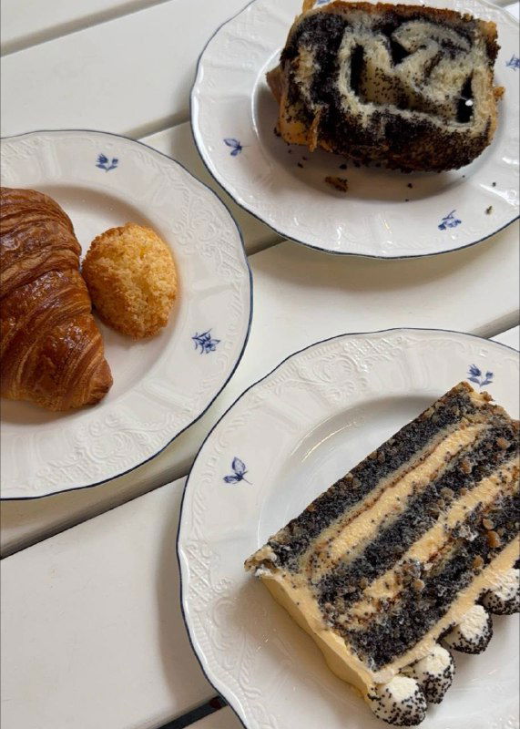 Кусочки пирога и круассаны на белых тарелках на столе — ассортимент сладкой выпечки и десертов в местной пекарне или кафе.