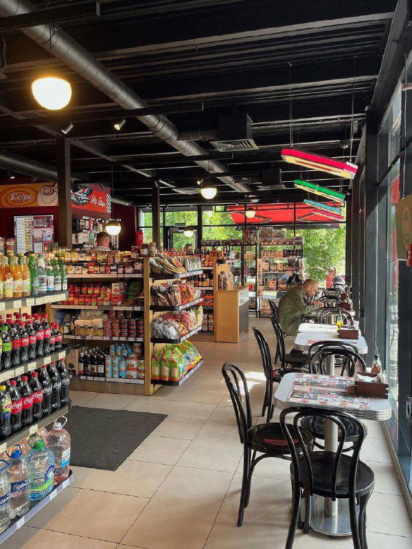 Интерьер мини-маркета при заправке: стеллажи с напитками и закусками, столики у окна — уютная зона для перекуса прямо у колонок.