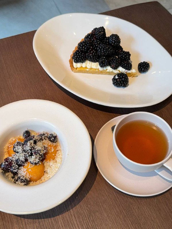 На десерт: хрустящие сырники с сезонными ягодами и миндальный тарт с маскарпоне на белых тарелках рядом с чашкой чая.