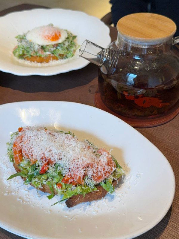 Тост с лососем и страчателлой крупным планом: зелень, тертый сыр и текстура хлеба на белой тарелке в Teya.