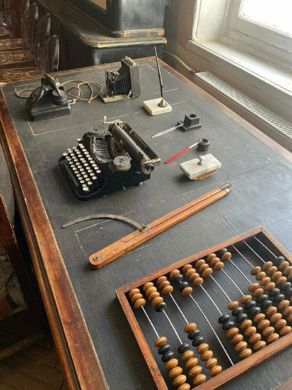 Старинный письменный стол в читальном зале: печатная машинка, телефон, счёты и чернильницы — музейные предметы, создающие атмосферу XIX века.