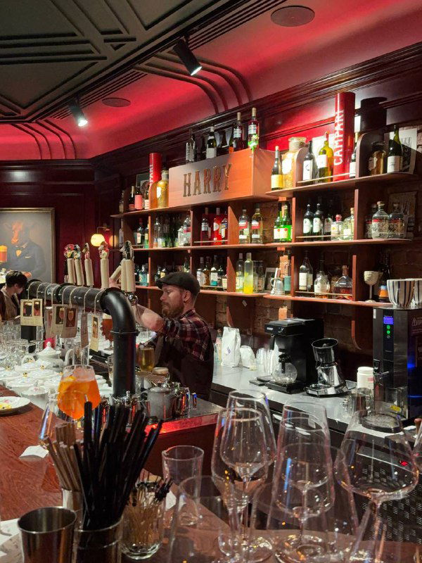Бармен за стойкой: крановое пиво, бокалы и множество бутылок на полках за баром, видна рабочая зона и фокус на разливе напитков в Harry Not Original.