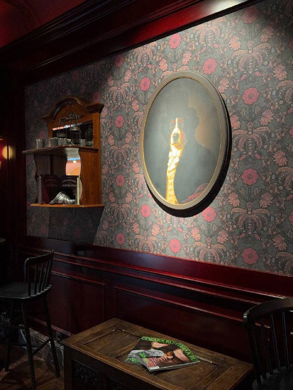 Атмосферный уголок с портретом на стене, тёмными обоями с узором и мягким креслом рядом — интерьерные акценты, подчеркивающие стиль заведения.