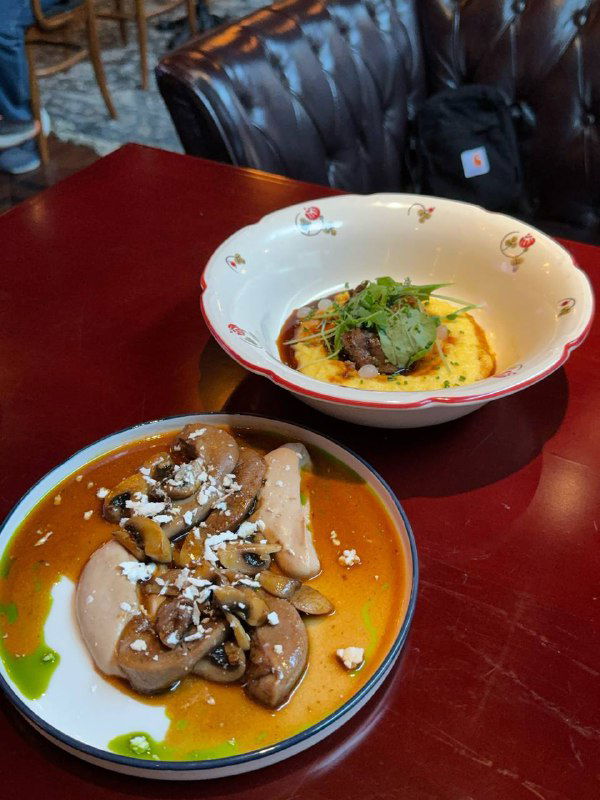 Тарелка с телячьими щечками и полентой, аккуратно поданная в белой глубокой посуде: видны кусочки мяса, пармезан и зелень для презентации блюда.