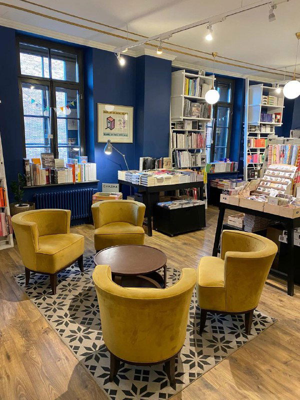 Комфортная зона чтения с круглыми столиками и ярко‑желтыми креслами на декоративном ковре — место для кофе и чтения в книжном.