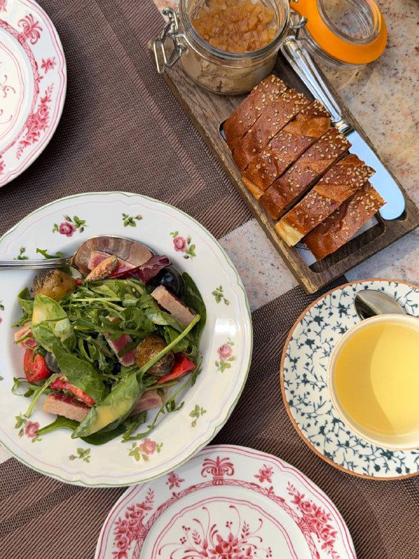 Тарелка с салатом Нисуаз и ломтиками хлеба на доске: свежие листья, тунец и стильная посуда на столе кафе.