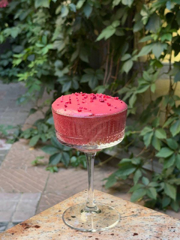 Яркий розовый десерт в высоком бокале на фоне зелёной листвы летней террасы — авторская сладкая подача в Claret.