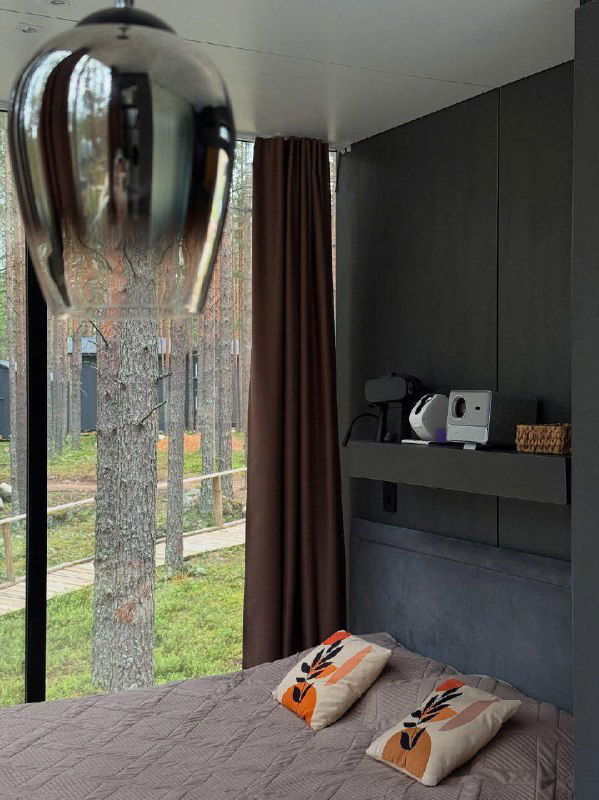 Интерьер домика с панорамным окном: полка с кофемашиной, декоративные подушки и вид на лес за стеклом — уютная перестановка для отдыха.