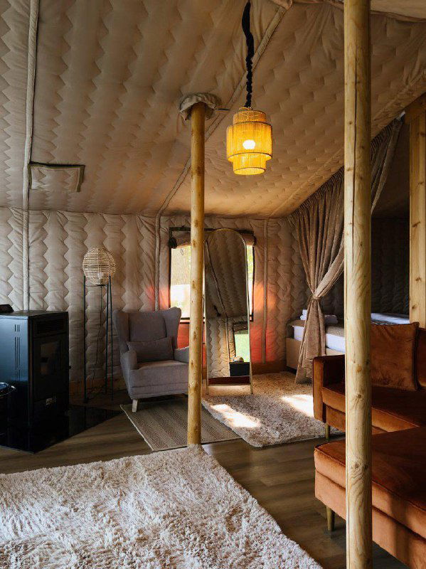 Просторный интерьер палаточного домика с деревянными опорами, ковриком и мягкой зоной — тёплые текстуры и светильник создают уютный ретритный антураж.
