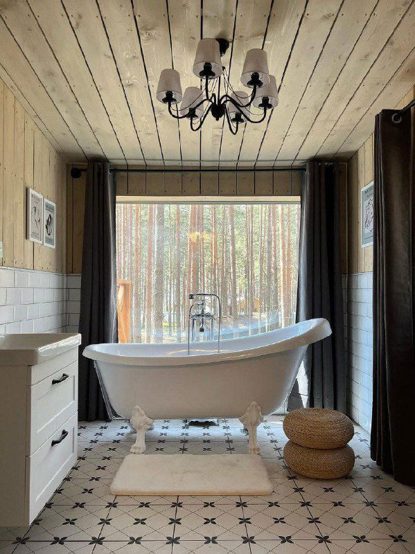 Светлая ванная с отдельностоящей чугунной ванной, керамогранитной плиткой и большим окном с видом на сосновый лес — сочетание ретро и современного стиля.