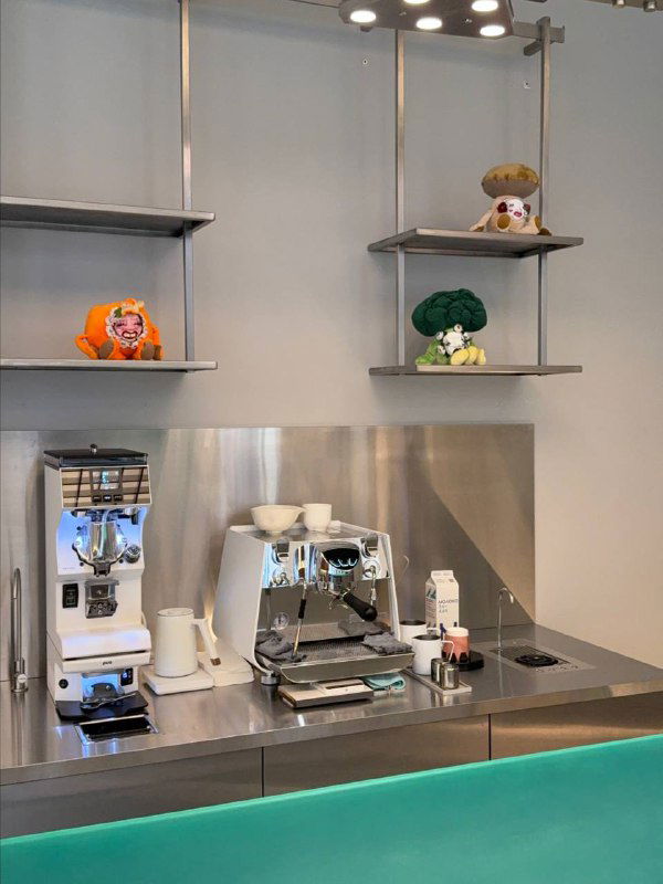 Кофейная станция в концепт‑сторе: профессиональная кофемашина, мельницы и чистая рабочая поверхность с бирюзовой передней панелью.
