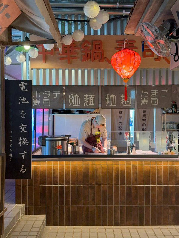 Барная зона и прилавок TAO: повар за стойкой, вывески с иероглифами и подсветка в паназиатском стиле на фоне кухни