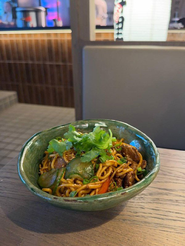 Чаша wok-лапши с говядиной, зеленью и хрустящими добавками — тёплая порция в глубокой миске на столе ресторана TAO