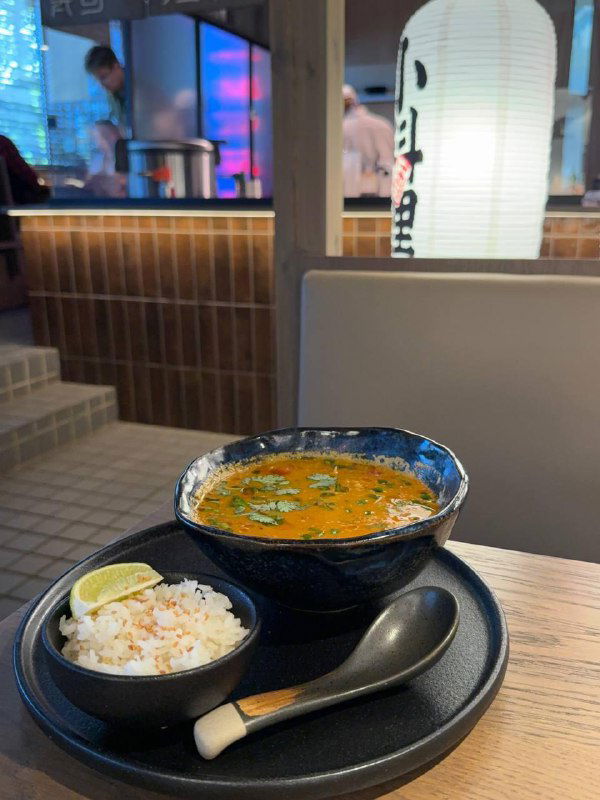 Том ям с морепродуктами в глубокой тарелке и миска риса с долькой лайма — классическая подача супа в TAO на фоне интерьера