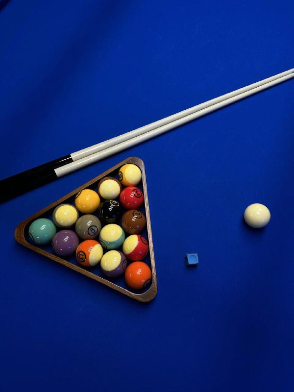 Крупный план треугольника цветных шаров на синем сукне, кий и мел рядом — подготовка к партии в SeaWolves, съёмка с акцентом на оборудование.