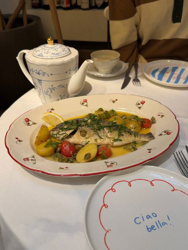 Горячее блюдо — дорада аква-пацца на тарелке с лимоном, оливками и зеленью; размер порции рассчитан примерно на двоих.