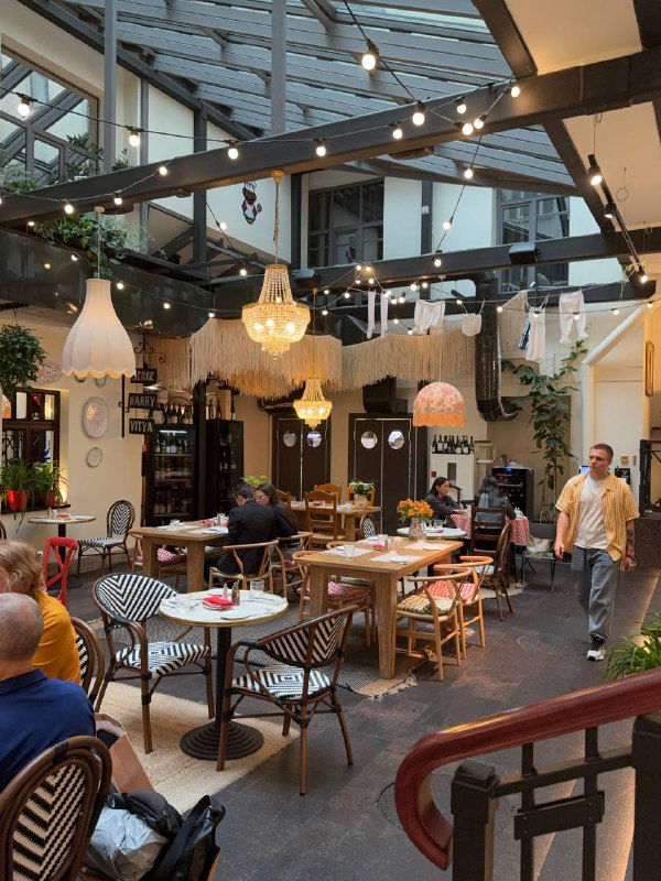Общий вид зала Mia Strada под стеклянной крышей: столики, декор, лампы и гости — тёплая дневная/вечерняя атмосфера заведения.