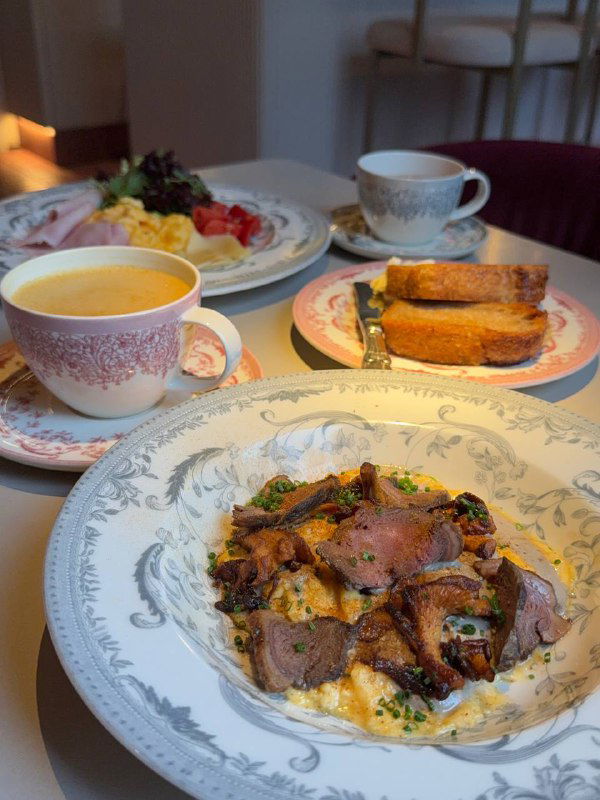 Стол с несколькими завтраками в Futurist: тарелки со скрэмблом, ломти хлеба и чашки с напитками — крупный план сервировки.