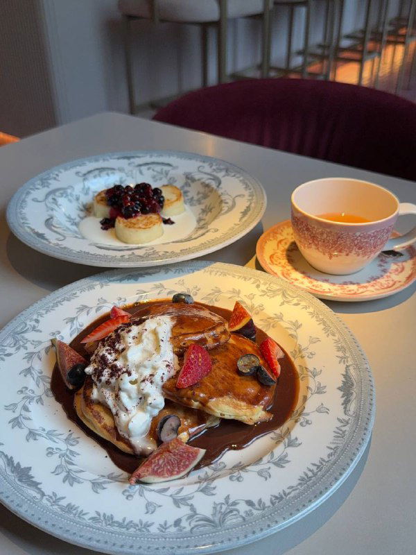 Оладьи с ягодами, страчателлой и ореховым соусом на фарфоровой тарелке — тёплые тона и аппетитная подача в кафе Futurist.