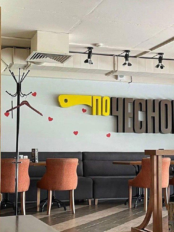 Интерьер сети «По чесноку» с логотипом на стене, столами и стульями — на фото видно фирменную стилистику и атмосферу заведения.