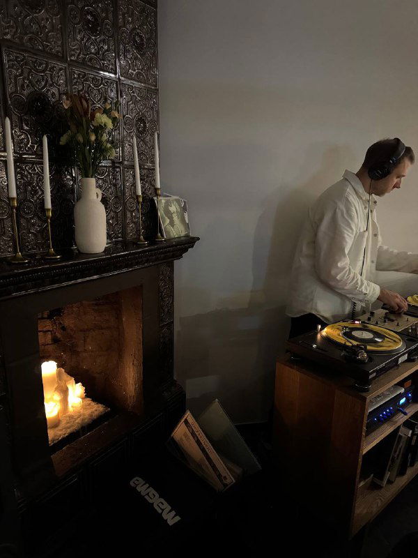 Фрагмент камина с горящими свечами и диджей в светлой рубашке у пульта — уютная сценография вечера в бистро.