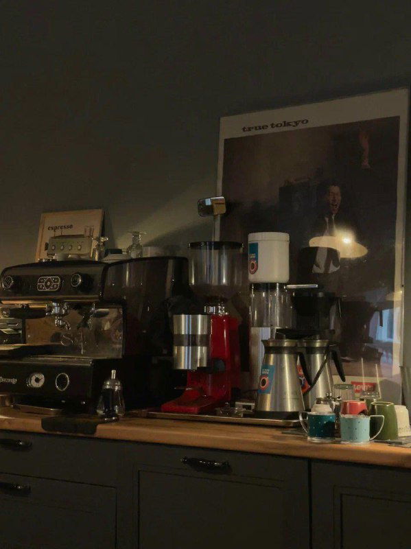 Кофейная техника и аксессуары на тёмном фоне, чашки и кувшин — вид рабочей зоны кофейни с акцентом на ретро-стиле и уютной сервировке.