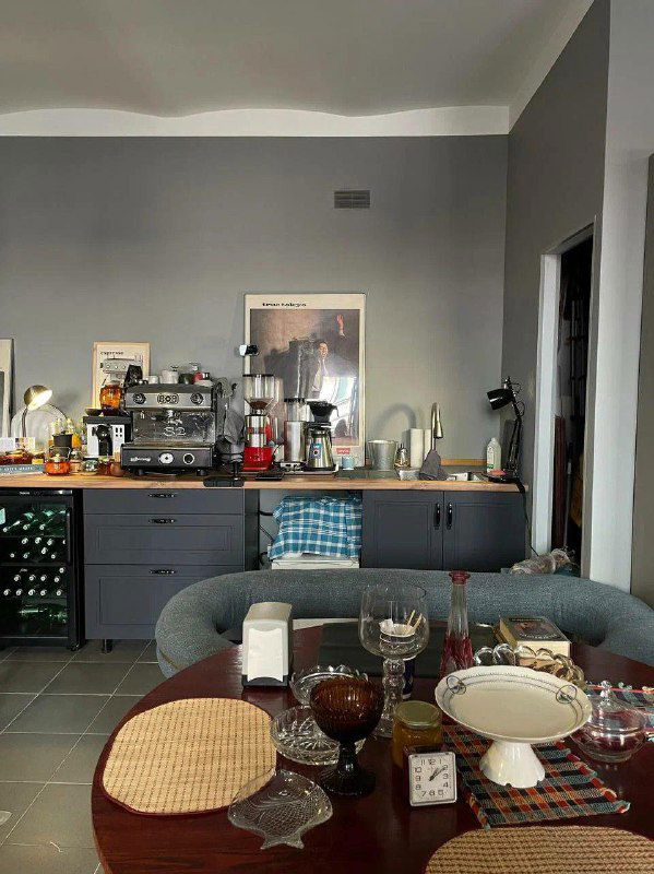 Общий вид столовой зоны с сервировкой, стеклянной посудой и мебелью в мягких тонах — интерьер винтажного магазина-кофейни с домашней атмосферой.