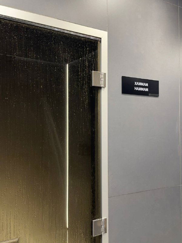 Дверь с табличкой «хамам» на тёмной стене — вид на вход в парную зону спа с минималистичной отделкой и влажной атмосферой.