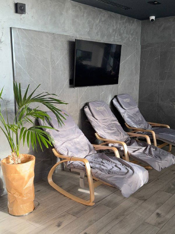 Несколько массажных кресел в спокойной зоне отдыха с растениями и телевизором — интерьер в серо‑деревянных тонах для релакса.