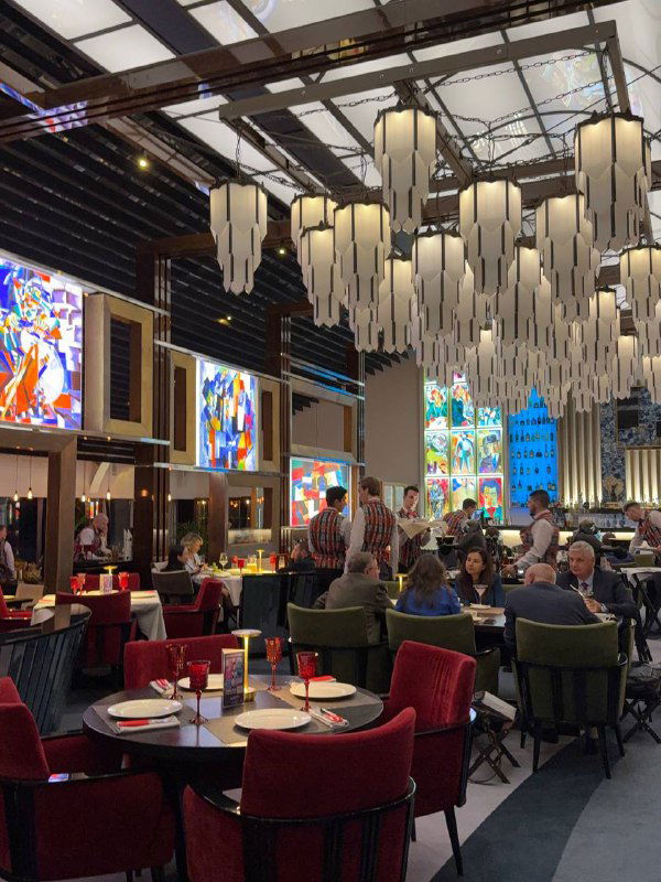 Общий план зала ресторана «Блок»: гости за столиками, высокая декоративная люстра и яркие настенные панно создают праздничную атмосферу