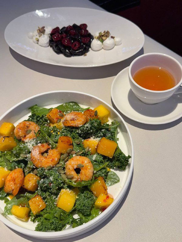 Салат с печёной тыквой и северными креветками на белой тарелке: яркие кусочки тыквы, креветки и зелёные листья на фоне белой скатерти