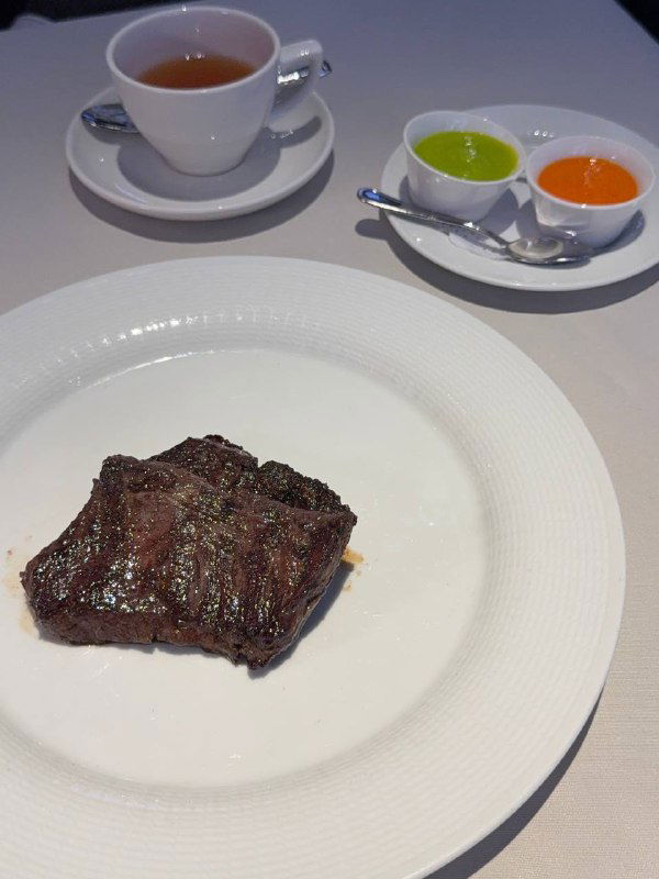 Стейк Эспадрон на белой тарелке: прожарка и текстура мяса видны на фоне минималистичной сервировки и чашки чая