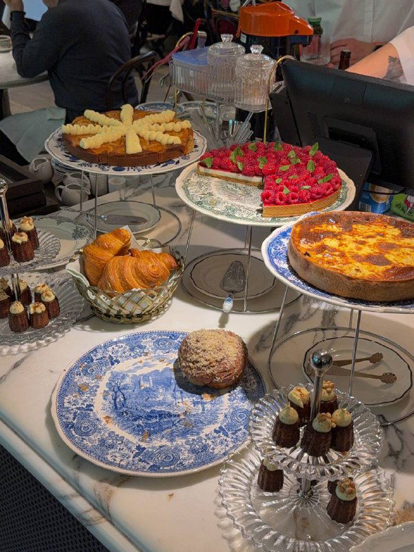 Витрина с десертами и выпечкой на этажерке: торты, пирожные и печенье на фоне узнаваемой синей фарфоровой посуды ресторана.