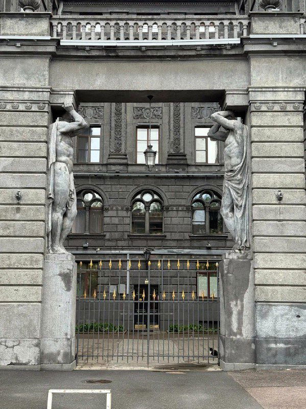 Входная арка и ворота доходного дома Роберта Веге с двумя атлантами по бокам: симметрия, металлические шипы на воротах и фактура стен в кадре.