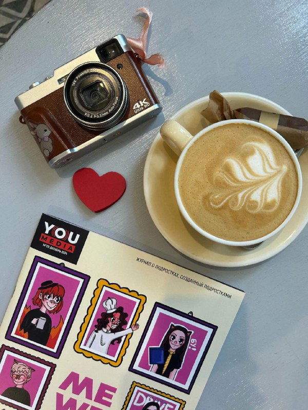 Столик в книжном: спешелти-латте с рисунком, ретро-фотоаппарат и журнальный разворот — уютная сцена для неспешного чтения и съёмки в кафе-магазине