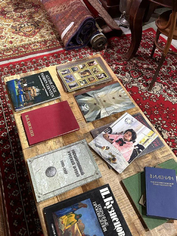 Ковёр и стол с разложенными старинными книгами, фотоальбомами и бумажными документами — уголок с коллекционными изданиями и артефактами.