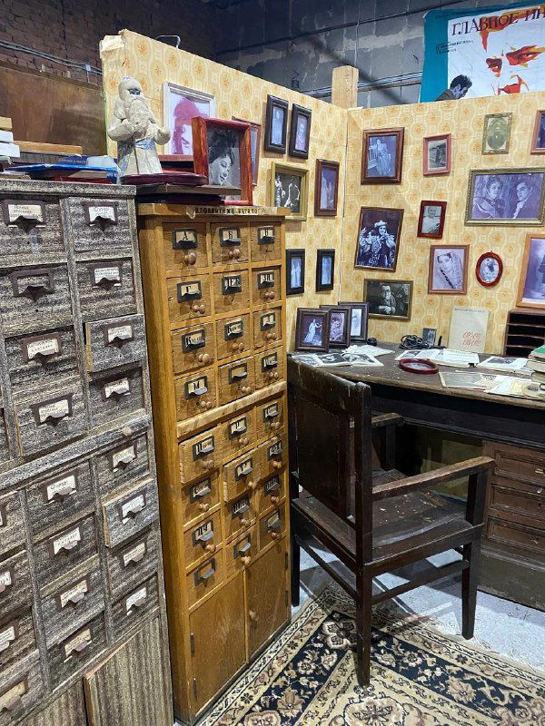 Уголок магазина с деревянными шкафчиками для мелочей, стулом и множеством рам, создающий ощущение старинного склада и архива предметов.