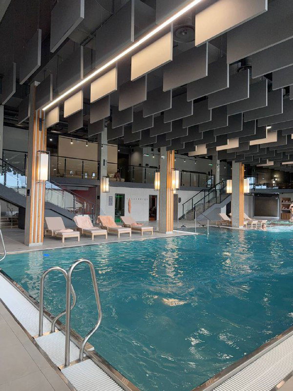 Крытый бассейн комплекса Green Flow: вода, лестница у бортика, шезлонги по периметру и современная архитектура зала с высокими потолками.