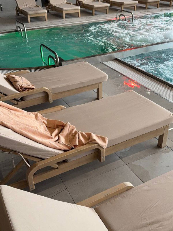 Зона у бассейна с шезлонгами и простынями, гидромассажные ванны и спокойная плиточная отделка — место для релакса после процедур.