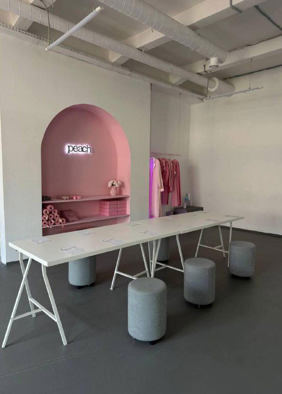 Стильная зона ресепшн и коворкинг‑пространство в светлых тонах: белые столы, стойка с брендингом Peach и минималистичные табуреты.