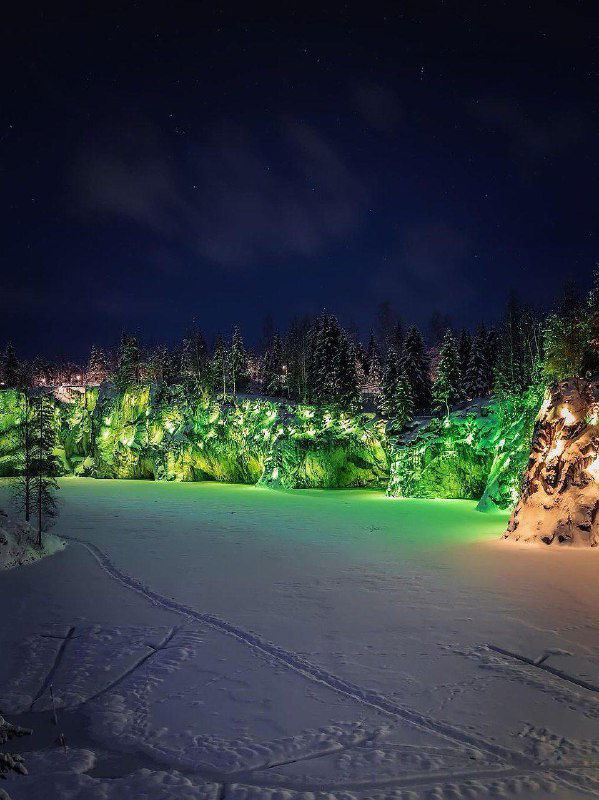 Ночной вид Рускеальского каньона с зелёной подсветкой, замерзшая вода и следы на снегу, зелёные световые акценты.