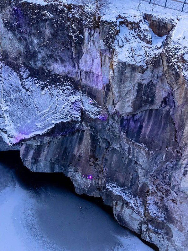 Вертикальная часть гранитной стены карьера Рускеала с фиолетовыми и зелёными прожекторами, текстура камня и снег.