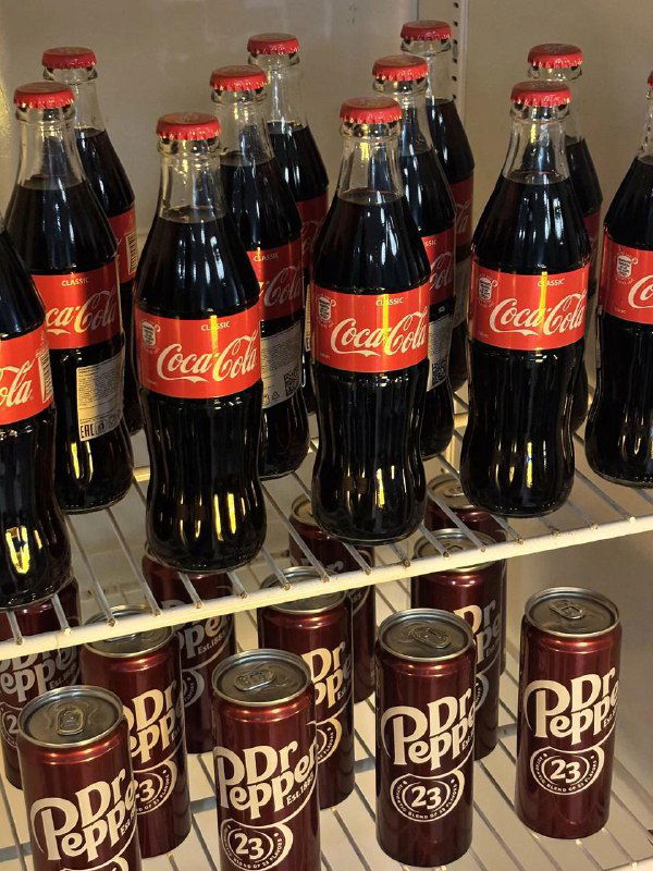 Полка с бутылками Coca‑Cola и банками Dr Pepper в холодильнике киноснеков — ассортимент напитков, предлагаемых в кинотеатре-кафе.