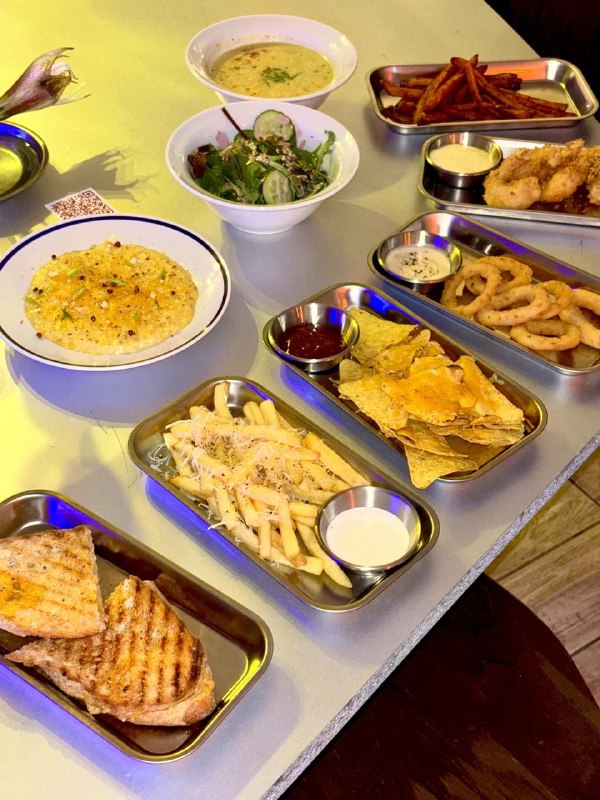 Лотки со снеком и закусками: картофель фри, кольца кальмара, салаты и горячие блюда, сервированные на металлических подносах.