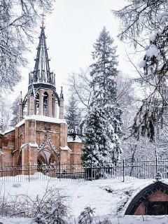 Готическая церковь среди заснеженных деревьев в парке: кирпичная архитектура, зимняя окантовка из снега и тихие дорожки вокруг.