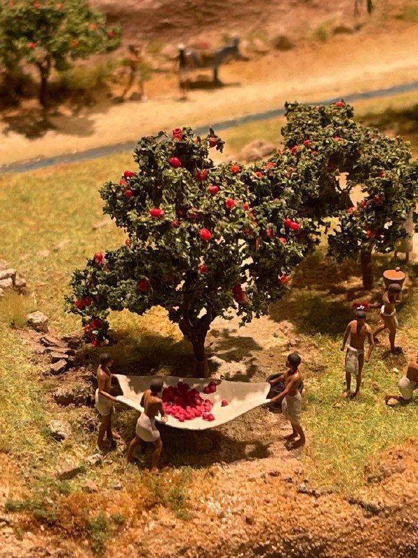 Крупный план миниатюрной сцены с деревом и людьми, разворачивающими бытовую сцену — акцент на деталях повседневной жизни в макете.