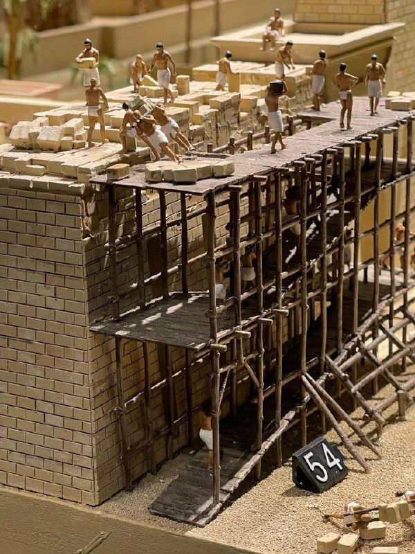 Миниатюрные строители на строительной площадке древнего города в макете: леса, рабочие и блоки стен в крупном подробном масштабе.