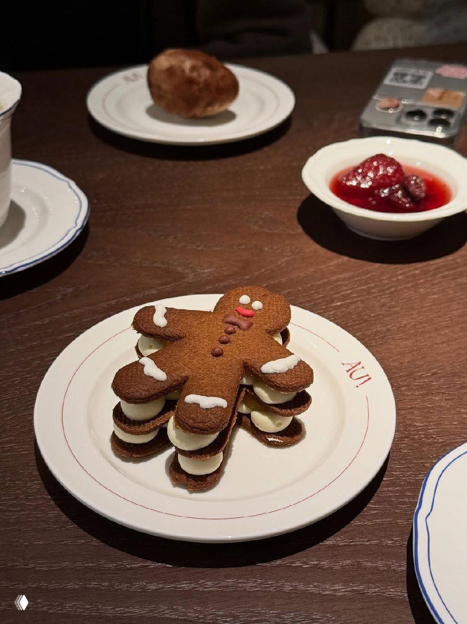 Десерт в форме пряничного человечка с кремовыми прослойками на тарелке с логотипом Au Delà — крупный план сладкого угощения в кафе.