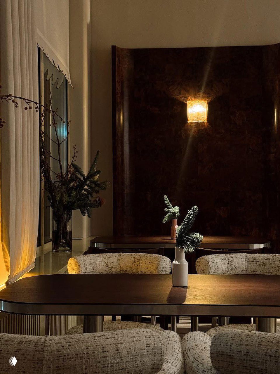 Сцена с сервированными столами и небольшой вазой в центре, мягкие кресла и тёплое акцентное освещение в зале ресторана.